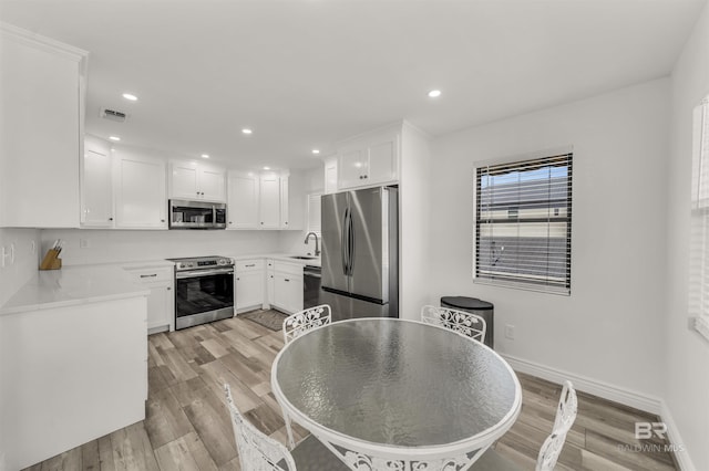 kitchen with backsplash, stainless steel appliances, sink, light hardwood / wood-style flooring, and white cabinetry