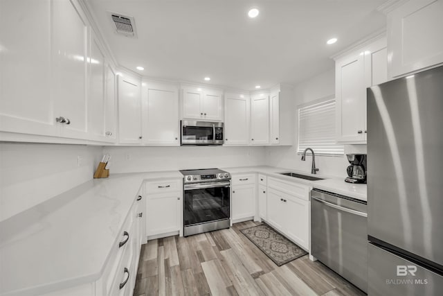 kitchen featuring white cabinetry, sink, light stone counters, light hardwood / wood-style flooring, and appliances with stainless steel finishes