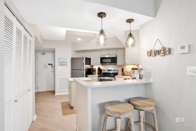 kitchen featuring kitchen peninsula, a kitchen breakfast bar, stainless steel appliances, pendant lighting, and light hardwood / wood-style flooring