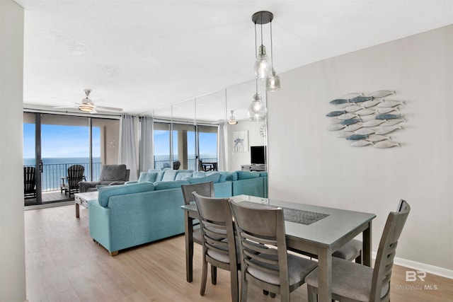 dining area with a water view, light hardwood / wood-style flooring, expansive windows, and ceiling fan