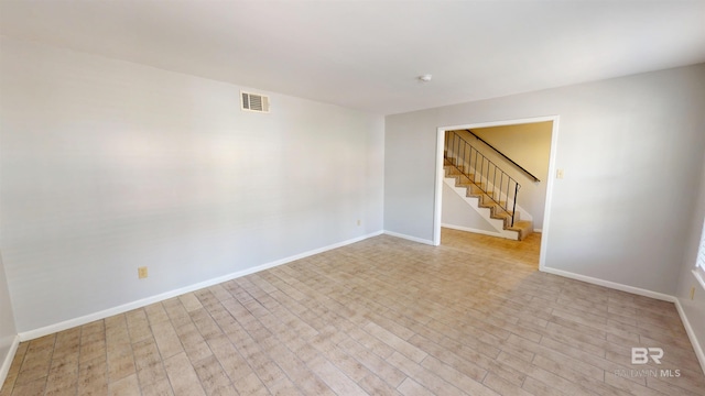 empty room with stairway, baseboards, wood finished floors, and visible vents