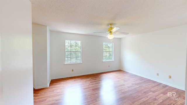 spare room featuring baseboards, a ceiling fan, light wood-type flooring, and a textured ceiling