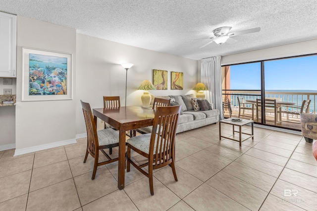 dining area with a water view, ceiling fan, light tile patterned floors, and a textured ceiling