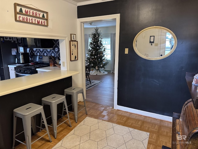 kitchen with stainless steel gas range oven, a kitchen bar, and parquet floors