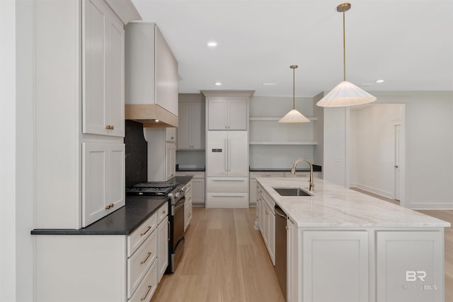 kitchen with appliances with stainless steel finishes, dark stone counters, light hardwood / wood-style flooring, sink, and decorative light fixtures