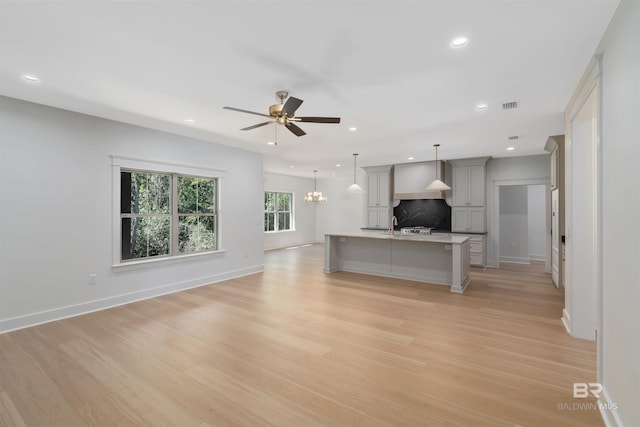 unfurnished living room with ceiling fan with notable chandelier and light wood-type flooring