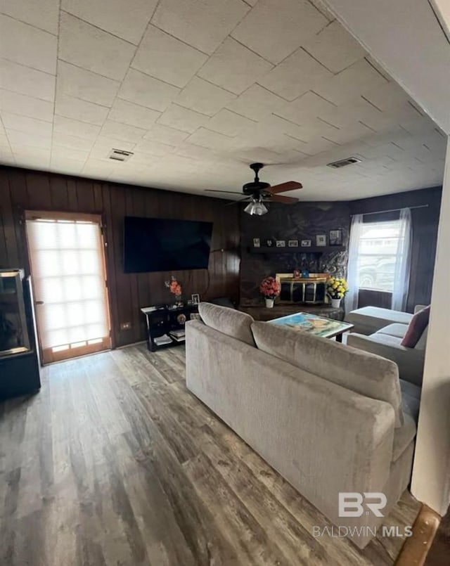 living room with hardwood / wood-style flooring, wooden walls, and ceiling fan