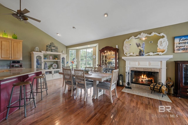 dining space featuring a tile fireplace, vaulted ceiling, dark hardwood / wood-style floors, and ceiling fan