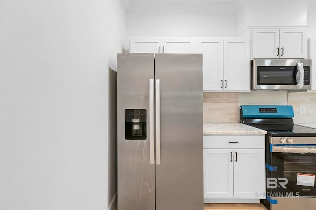 kitchen with white cabinets, tasteful backsplash, light stone countertops, and appliances with stainless steel finishes