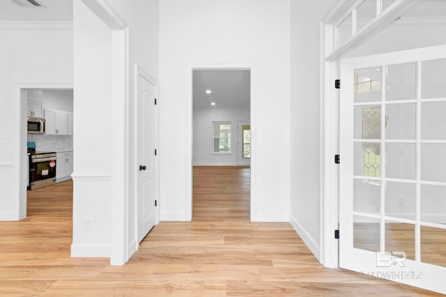 hall with baseboards, light wood finished floors, and visible vents