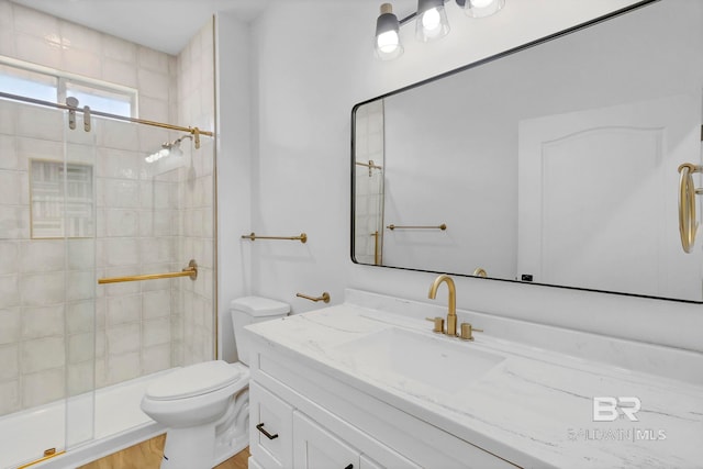 bathroom with vanity, toilet, tiled shower, and wood finished floors
