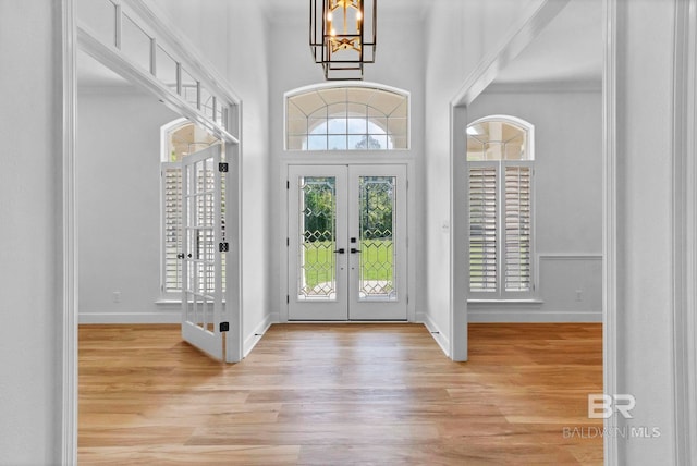 foyer featuring french doors, a towering ceiling, a notable chandelier, and light wood finished floors