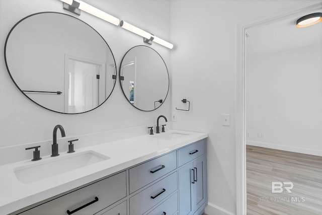 bathroom with double vanity, a sink, baseboards, and wood finished floors