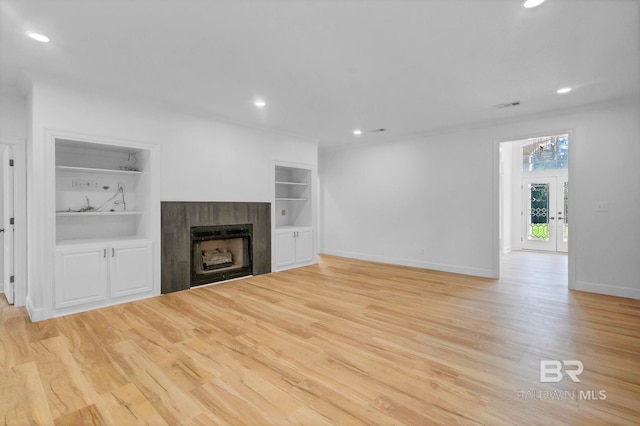 unfurnished living room with a tile fireplace, baseboards, built in shelves, recessed lighting, and light wood-type flooring
