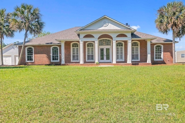greek revival house featuring french doors, brick siding, a front yard, and a shingled roof