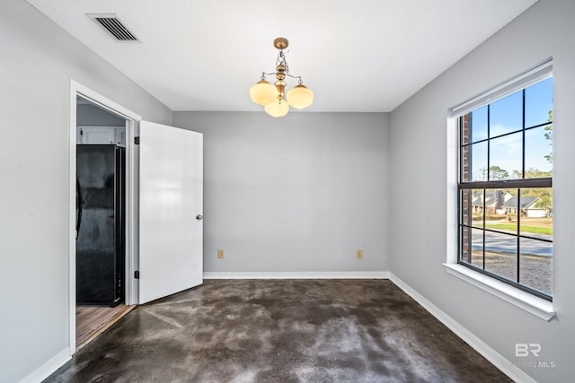 spare room featuring a notable chandelier, plenty of natural light, and concrete floors