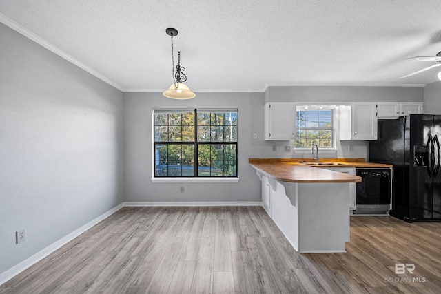 kitchen featuring decorative light fixtures, black appliances, kitchen peninsula, white cabinetry, and butcher block counters