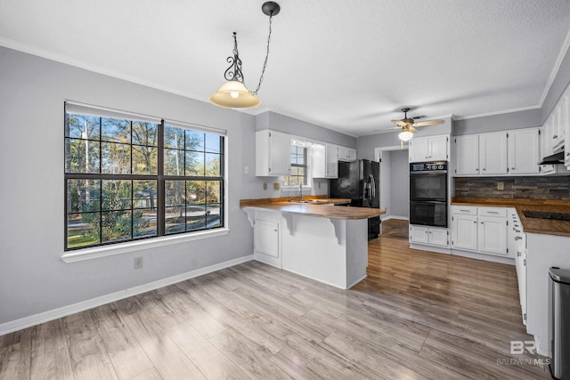 kitchen with black appliances, decorative light fixtures, wood counters, and white cabinetry