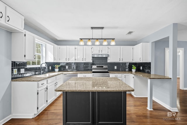 kitchen with appliances with stainless steel finishes, white cabinetry, sink, a center island, and light stone countertops