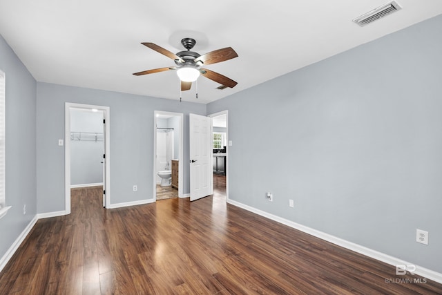 unfurnished bedroom featuring ensuite bathroom, dark hardwood / wood-style flooring, a walk in closet, ceiling fan, and a closet