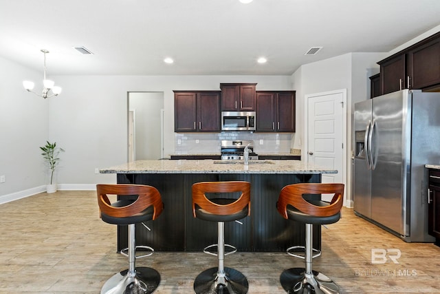 kitchen featuring a kitchen island with sink, stainless steel appliances, light stone countertops, and light hardwood / wood-style floors