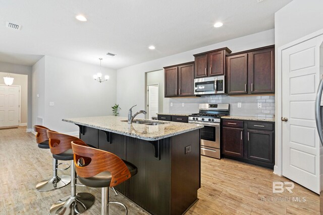 kitchen with light stone countertops, a kitchen island with sink, light hardwood / wood-style floors, stainless steel appliances, and sink