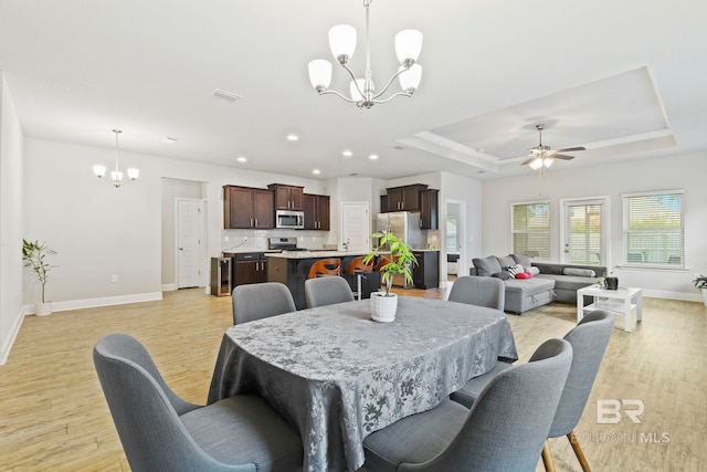 dining area featuring a tray ceiling, ceiling fan with notable chandelier, and light hardwood / wood-style flooring