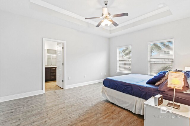 bedroom with a raised ceiling, ensuite bath, wood-type flooring, and ceiling fan