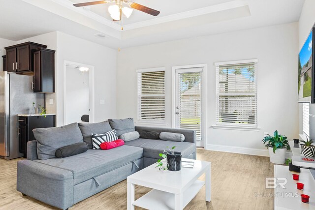 living room with light wood-type flooring, a raised ceiling, and ceiling fan