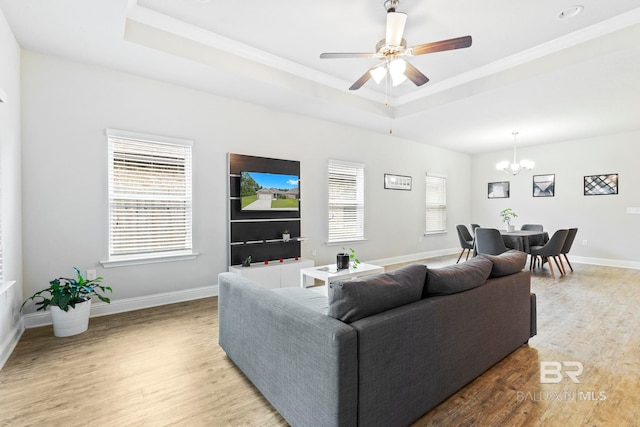 living room featuring a wealth of natural light, a tray ceiling, ceiling fan with notable chandelier, and hardwood / wood-style flooring