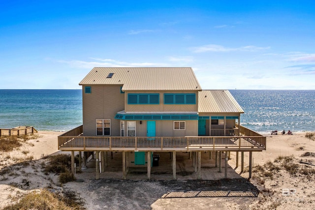 back of house with a deck with water view and a beach view