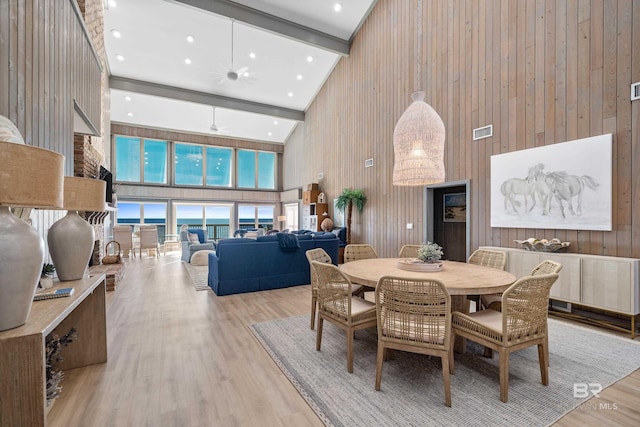 dining area featuring high vaulted ceiling, wooden walls, beam ceiling, ceiling fan, and light wood-type flooring