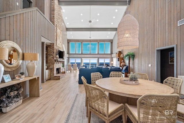 dining space featuring wooden walls, a large fireplace, a high ceiling, and light wood-type flooring