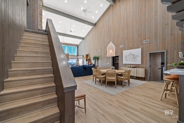 dining room featuring beam ceiling, high vaulted ceiling, light hardwood / wood-style floors, and wood walls