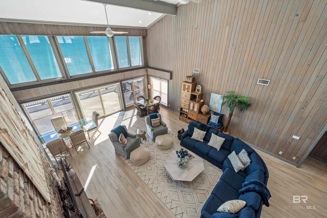 living room with hardwood / wood-style floors, high vaulted ceiling, wood walls, ceiling fan, and beam ceiling