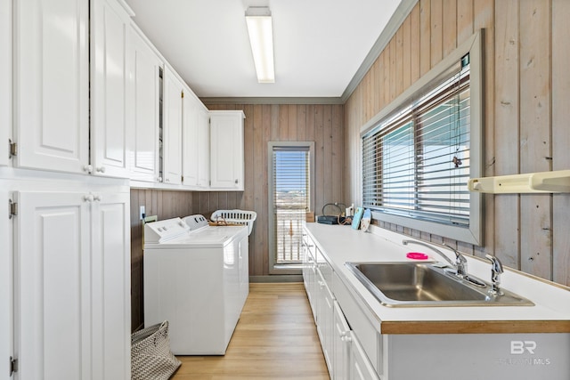 clothes washing area with wooden walls, sink, cabinets, washing machine and dryer, and light hardwood / wood-style flooring