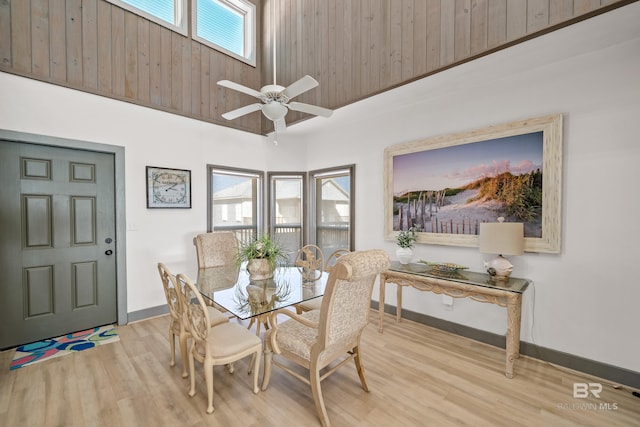 dining room with ceiling fan, a towering ceiling, and light wood-type flooring