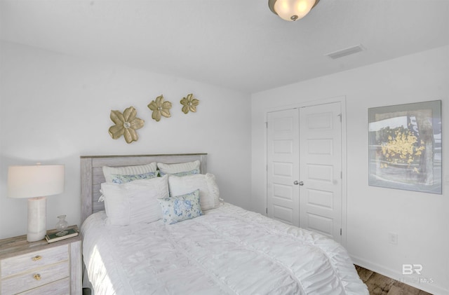 bedroom with wood finished floors, visible vents, and a closet