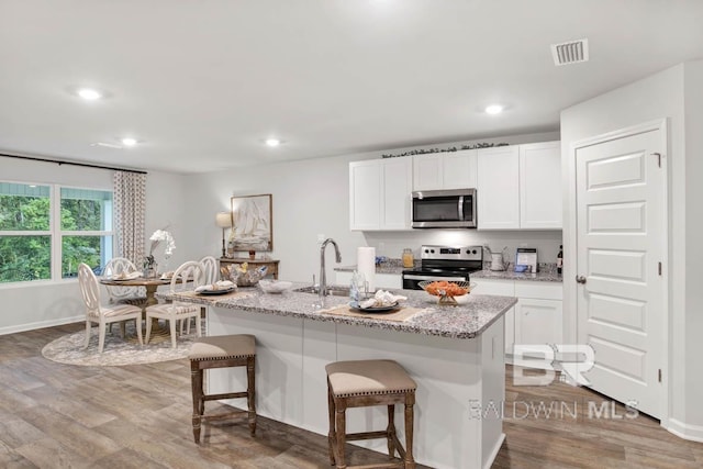 kitchen with a breakfast bar area, visible vents, appliances with stainless steel finishes, and wood finished floors