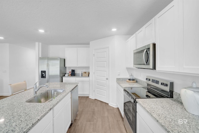 kitchen featuring light wood-type flooring, appliances with stainless steel finishes, white cabinets, a textured ceiling, and a sink