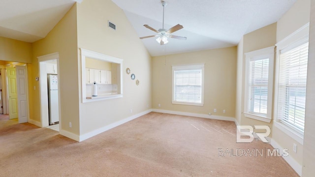 carpeted empty room with ceiling fan, a healthy amount of sunlight, and vaulted ceiling