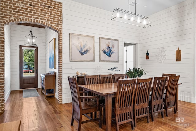 dining space with arched walkways, track lighting, hardwood / wood-style flooring, and a notable chandelier