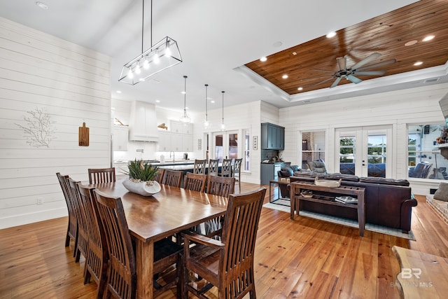 dining room with light wood-style floors, a tray ceiling, and french doors