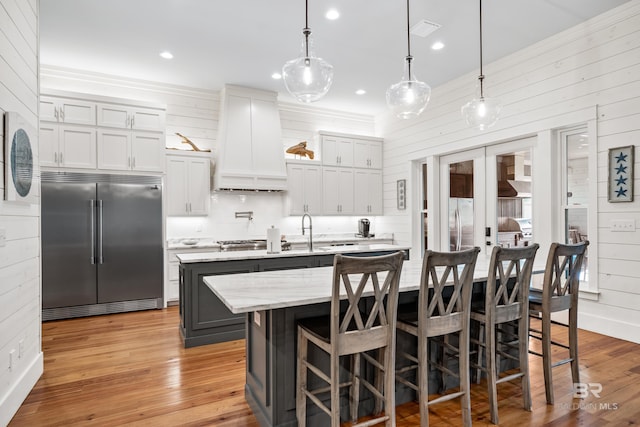 kitchen with an island with sink, light wood-style floors, premium range hood, and appliances with stainless steel finishes