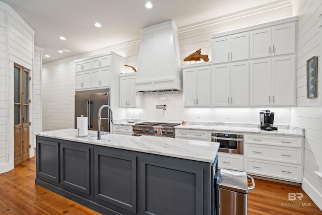 kitchen with gray cabinets, light wood-style flooring, white cabinets, high quality appliances, and premium range hood