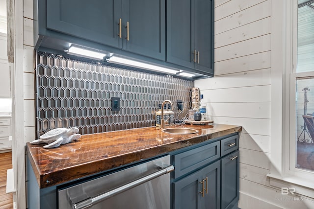 kitchen featuring stainless steel dishwasher, wood walls, a sink, and blue cabinets