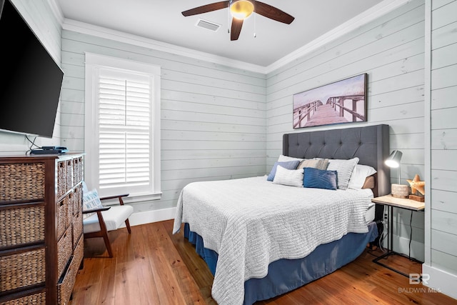 bedroom with hardwood / wood-style flooring, baseboards, visible vents, and crown molding