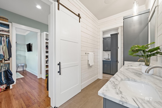 full bath with wood finished floors, a sink, ornamental molding, double vanity, and a walk in closet