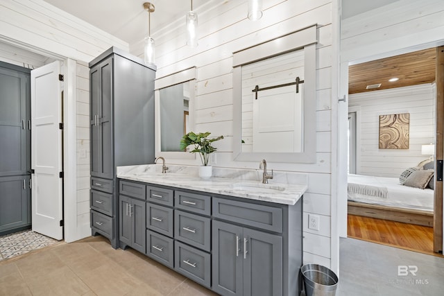 full bath featuring double vanity, wood walls, tile patterned flooring, and a sink