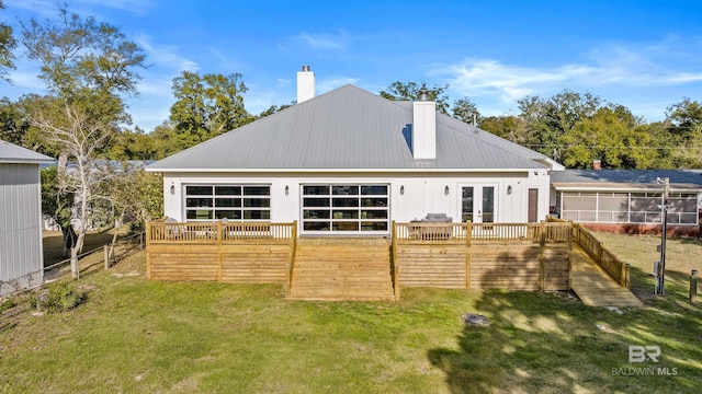 back of house featuring metal roof, french doors, a lawn, a wooden deck, and a chimney